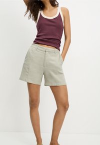 Bordowy top na ramiączkach z kremową lamówką i dopasowanym krojem, zestawiony z jasnobeżowymi szortami z bocznymi kieszeniami o gładkim, fakturowanym wykończeniu.