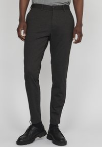 Mörkgrå skräddarsydda byxor i texturerad tyg, med knappstängning och sidfickor, tillsammans med svarta snörskor.