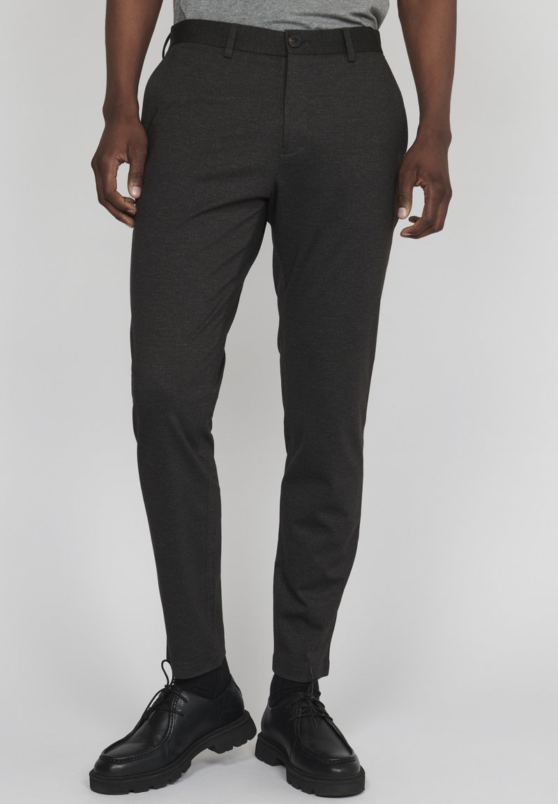 Mörkgrå skräddarsydda byxor i texturerad tyg, med knappstängning och sidfickor, tillsammans med svarta snörskor.
