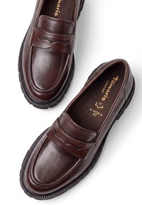 Paire de mocassins en cuir marron foncé avec semelles noires épaisses, lanière décorative sur le dessus, étiquetés large largeur taille 37 à l'intérieur.