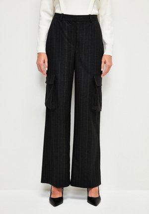 Pantalones de pierna ancha a rayas negras con dos bolsillos cargo frontales, fabricados en una tela texturizada. Combinados con unos tacones negros de punta afilada.
