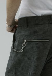 Gray textured pants featuring a back zip pocket and a silver chain attachment. The fabric has a subtle check pattern and a fitted waist.