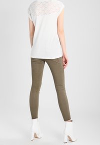 Top corto bianco a maniche corte con schiena in pizzo strutturato, abbinato a pantaloni aderenti verde oliva e stivaletti bianchi con tacco.