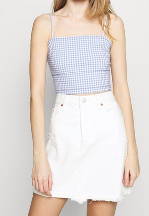 Frau trägt ein blau-weiß kariertes, bauchfreies Tanktop und einen hoch taillierten weißen Jeansrock mit ausgefranstem Saum.