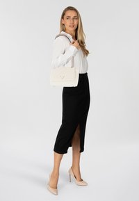 Borsa a tracolla trapuntata di colore crema con catena, design rettangolare, con accentuazione in metallo del logo, abbinata a una gonna nera con spacco laterale.