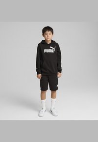 Crna dukserica s bijelim logotipom "PUMA", crne kratke hlače, bijele čarape i bijele tenisice. Ima kengursku džep i kapuljaču.