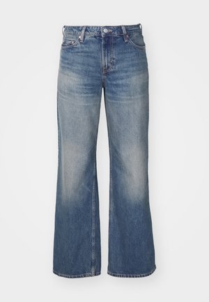 Jean en denim bleu clair avec un design à jambes larges, présentant un délavage, cinq poches et un zip à bouton. Surpiqûres détaillées le long des coutures.