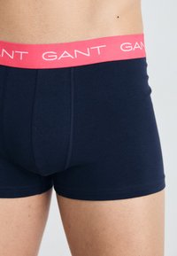 Tengerészkék boxeralsó rózsaszín rugalmas derékkal, amelyen fehér színnel van nyomtatva a "GANT" márkaneve. Simlény és rugalmas anyag a kényelem érdekében.