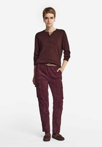 Burgundy kofta med knappstängning, långa ärmar och avslappnad passform, i kombination med matchande cargobyxor och bruna skor. Slät textur genom hela plagget.