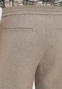 Bruine textuurbroek heeft een gladde afwerking, een elastische tailleband en twee achterzakken met een minimalistisch design.