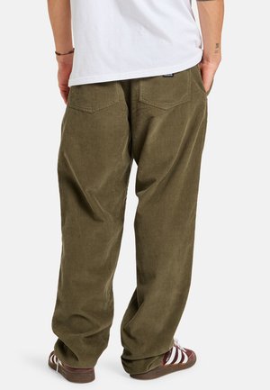 Olive green corduroy pants with a relaxed fit, featuring two back pockets and visible ribbed texture. Worn with brown striped shoes.