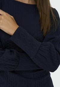 Námořnický modrý svetr s texturou a vzorem copánkového pletení, s dlouhými rukávy a kulatým výstřihem. Měkká, silná tkanina s žebrovanými manžetami.