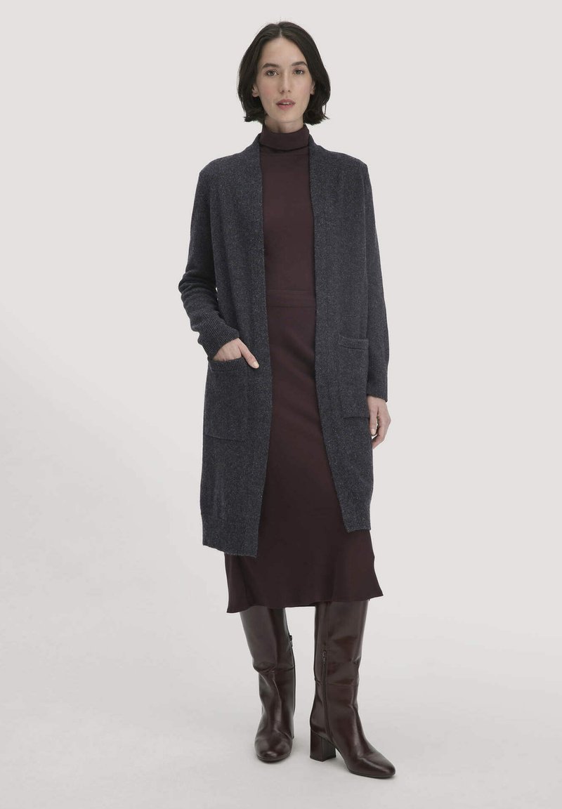 Langer, dunkelgrauer Cardigan aus weichem Material, mit offenem Vorderteil, langen Ärmeln und zwei Fronttaschen, getragen über einem dunklen Kleid und Stiefeln.