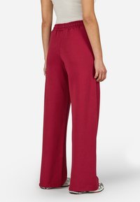 Široké nohavice vyrobené z mäkkého, elastického materiálu v hlbokej burgundskej farbe. Vyznačujú sa elastickým pásom a zúženými lemami.