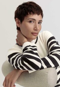 Strickpullover mit schwarz-weißen horizontalen Streifen, strukturierten Ärmeln, Rundhalsausschnitt und einem weichen hellen Hintergrund.