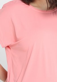 Camiseta de manga corta de color rosa claro, fabricada en tejido suave. Presenta un escote redondo y un corte holgado con aberturas a los lados para mayor comodidad.