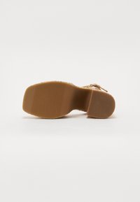 Sandal featuring a floral pattern on the upper, a flat sole with ribbed texture, and a light brown rubber outsole.