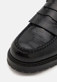 Scarpe nere in pelle con una texture liscia e lucida, caratterizzate da un design cucito e una suola in gomma spessa. Accentate da cinturini sovrapposti.
