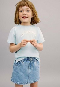 Vaaleansininen puuvillapaita, jossa tekstinä "Rakkaus tuoreisiin hedelmiin"; yhdistettyinä farkkuhameen kanssa. Lyhyet hihat, kaareva helma ja rento malli.