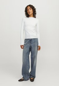 White ribbed long-sleeve top with scalloped hem paired with wide-leg blue denim jeans and black mesh flat shoes. Simple, casual outfit.