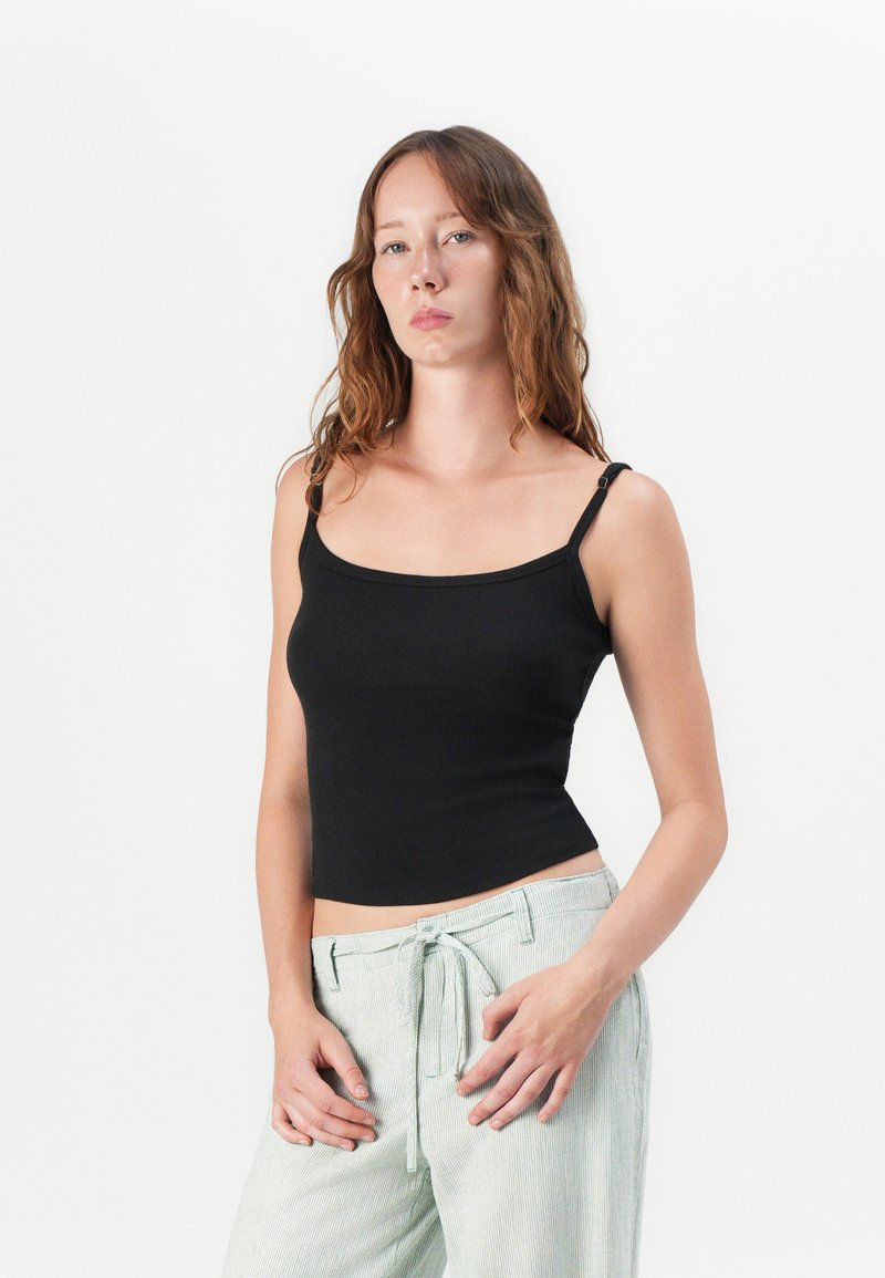 Czarny, żeberkowy top na ramiączkach z regulowanymi paskami, dopasowany krój, okrągły dekolt, w połączeniu z jasnoszarymi, fakturowanymi spodniami typu wide-leg.