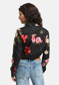 Blusa nera a fiori con motivi colorati di fiori rosa e rossi, maniche lunghe e colletto, abbinata a jeans di denim azzurri.