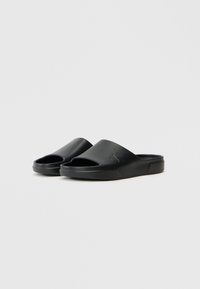 Black slide sandals with an open toe and curved upper, made of smooth material, featuring a subtle embossed logo on the side.