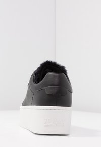 Černé kožené tenisky s platformovou podrážkou, které mají texturovanou bílou gumovou základnu a měkkou černou kožíškovou podšívku kolem límce.