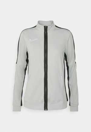 Helles graues Zip-Jackett mit schwarzen Seitenpaneelen, hohem Kragen und weißem Nike-Logo auf der Brust. Verfügt über eine glatte Textur und athletische Passform.