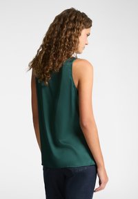 Top senza maniche verde realizzato in tessuto morbido, caratterizzato da un fitting comodo e una lieve caduta, con scollatura rotonda e orlo curvo sul retro.