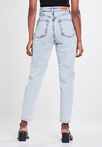 Jeans taille haute bleu clair en tissu denim. Texture déchirée, design à cinq poches et une étiquette en cuir de marque à l'arrière de la taille.