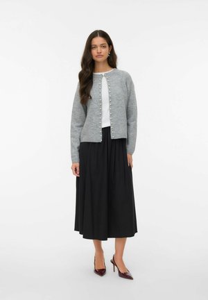 Gray button-up cardigan with pearls, worn over a white top and black pleated skirt. The outfit is complemented by burgundy high heels.