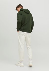 Green cotton hoodie with a drawstring hood, paired with light gray sweatpants featuring elastic cuffs and white sneakers.