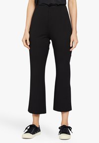 Zwarte, hoge taille flared broek van rekbaar materiaal, met een schone, zachte textuur en een aansluitende pasvorm, gecombineerd met zwarte sneakers.