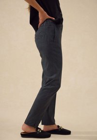 Pantaloni grigi a quadri con vestibilità comoda, caratterizzati da tasche laterali e una texture di tessuto liscia, abbinati a scarpe slip-on in pelle scamosciata nera.