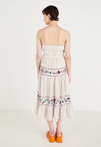 Strapless jurk tot de knie in gestreept wit en beige stof met bloemenborduursel. Heeft een geplooid lijfje en een gerimpelde zoom. Oranje sleehak sandalen.