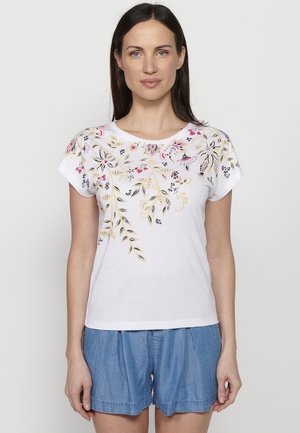 T-shirt blanc à manches courtes avec un motif floral en rose, bleu marine et jaune. Tissu doux et coupe décontractée, associé à un short en denim.