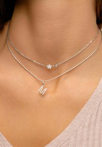Des colliers superposés en argent avec un charme en forme d'étoile et un pendentif étincelant en forme de lettre "M", mettant en valeur des designs de chaîne complexes et une finition polie.