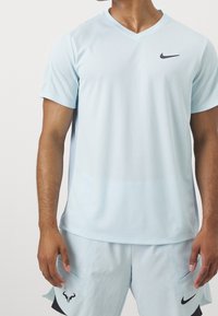 Hellblaues Sport-T-Shirt aus feuchtigkeitsableitendem Material, mit V-Ausschnitt und einem schwarzen Nike-Logo auf der Brust. Kurze Ärmel.