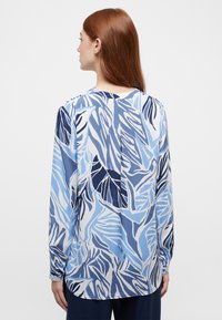 Langdurige blouse van lichtgewicht stof met een blauw-wit bladenpatroon. De achterkant toont een middennaad en knoopmanchetten.