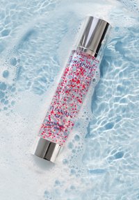 Gennemsigtig flaske med rensesgel med pink og hvide perler, sølv pumpehætte, mærket "Rensesgel" på fronten, placeret i sæbende blåt vand.
