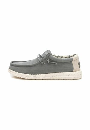 Zapato gris sin cordones con un upper de tejido texturizado, cordones elásticos y una suela blanca moteada. El interior presenta un forro con patrón.