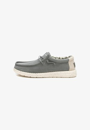Zapato gris sin cordones con un upper de tejido texturizado, cordones elásticos y una suela blanca moteada. El interior presenta un forro con patrón.