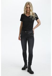 Črna majica z v-očesom v kombinaciji s temno modrimi skinny jeans hlačami. Hlače imajo sprednje žepke in zadrgo. Dopolnjeno s črnimi gležnjarji.