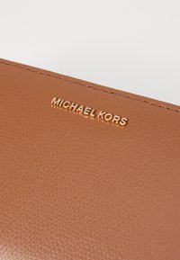 Brun lærpung med teksturert overflate, med en gullprydet "MICHAEL KORS" logo foran.