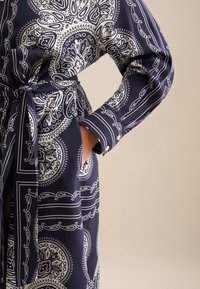 Abito blu navy con motivo paisley bianco, maniche lunghe e vita con fiocco, con tasche laterali e dettagli con bottoni sui polsini.
