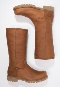 Hoge bruine leren laarzen met rubberen zolen, zichtbare stiksels en een ronde logo bij de hiel, geplaatst op een witte achtergrond.