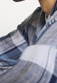 Rutigt skjorta i blått, grått och vitt med horisontella och vertikala linjer. Mjuk tyg med strukturerad krage och knappdetalj.