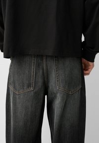 Tummat farkut, joissa on rento istuvuus, kahdella takataskulla ja kontrastivärisessä ompelussa. Kangas on hieman kuluneen näköinen.