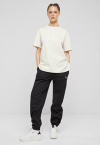 Kremfarvet oversized t-shirt med korte ærmer og broderet logo, parret med sorte joggers med elastisk talje og manchetter. Hvide sneaks.